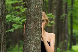 schön Mädchen spähen aus von hinter ein Baum im das Wald foto