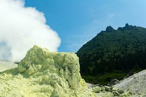 hell Rauchen Fumarole mit Schwefel Einlagen gegen das Hintergrund von das Mendeleev Vulkan Gipfel auf das Insel von Kunaschir foto