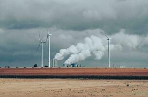 Wind Turbinen und industriell Rohre mit Rauch auf ein wolkig Tag im Deutschland foto