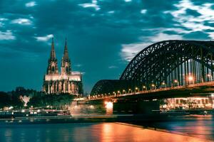 Köln Kathedrale und hohenzollern Brücke im das Abend mit Beleuchtung gegen wolkig Himmel foto