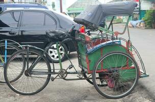 traditionell Rikscha oder becak ist geparkt Nächster zu ein Auto warten zum ein Kunde foto