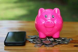 Rosa Schweinchen Bank auf das Stapel von Münzen thailändisch mit das Telefon platziert auf es ist Seite. foto