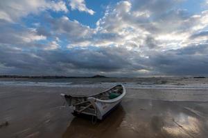 ein kleines Boot legte am bewölkten Strand an und der Himmel war mit dunklen Wolken bedeckt foto
