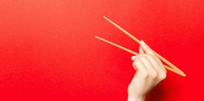 kreatives Bild von Holzstäbchen in weiblicher Hand auf rotem Hintergrund. japanisches und chinesisches essen mit kopierraum foto