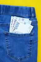 eben legen, Detail von Denim Jeans mit ukrainisch Griwna Rechnungen im Tasche auf Gelb Hintergrund. foto