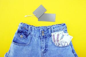 eben legen, Detail von Denim Jeans mit ukrainisch Griwna Rechnungen im Tasche mit grau Etikette auf Gelb Hintergrund. foto