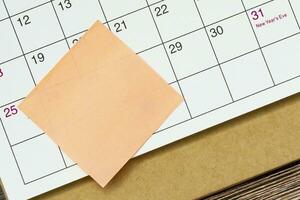 Orange Papier klebrig Hinweis und stecken zu ein Kalender Hintergrund. Erinnerung Konzept. foto