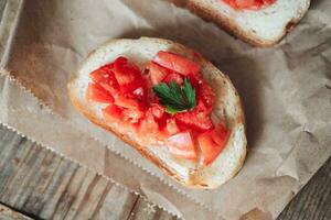 köstlich Bruschetta, getoastet Brot mit Tomaten auf Kunst Papier, auf ein hölzern Hintergrund foto