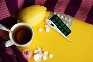 Tasse von Tee mit Zitrone mit Tabletten und ein Thermometer auf ein Gelb Hintergrund. foto