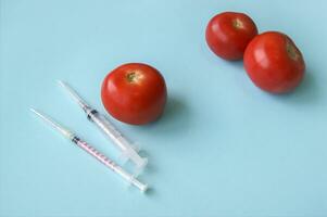 Tomate und Spritze mit gmo auf ein Blau Hintergrund. foto