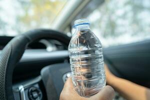 asiatische Fahrerin, die eine Flasche zum Trinken von Wasser hält, während sie ein Auto fährt. Wärmflasche aus Kunststoff verursacht Feuer. foto