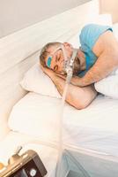 Schlafender Mann mit chronischen Atemproblemen erwägt die Verwendung der CPAP-Maschine im Bett. Gesundheitswesen, obstruktive Schlafapnoe-Therapie, CPAP, Schnarchkonzept foto