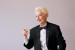 Stilvolle reife Sommelier-Senior-Frau im Smoking mit Glas Sekt. Spaß, Party, Stil, Lifestyle, Alkohol, Feierkonzept foto