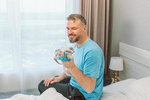 Reifer glücklicher Mann mit chronischen Atemproblemen erwägt, mit einer CPAP-Maschine auf dem Bett im Schlafzimmer zu sitzen. Gesundheitswesen, CPAP, Schnarchkonzept foto