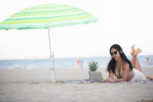 Frauen, die Bikinis tragen, benutzen Laptop für die Arbeit und hören im Sommer Musik am Strand. foto