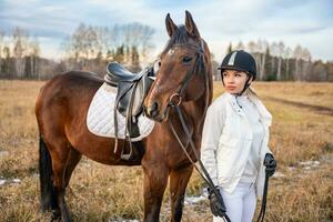 blond Fachmann weiblich Jockey Stehen in der Nähe von braun Pferd im Feld. Freundschaft mit Pferd. hoch Qualität Foto