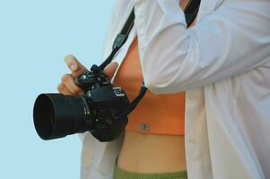 ein Mädchen Fotograf hält ein Kamera im ihr Hand. ein Fachmann Kamera im das Hände von ein Frau im ein Weiß Hemd auf ein Blau Hintergrund. foto