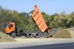 das Dump LKW entlädt Schutt. das LKW abgeladen das Ladung. Sand und Kies. Konstruktion von Straßen foto