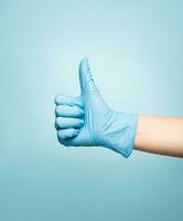 Hand im medizinisch Handschuh zeigen Daumen hoch. isoliert auf Blau Hintergrund. Medizin Konzept foto