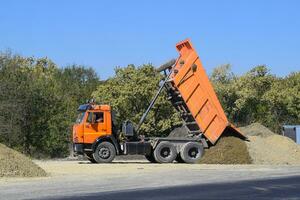 das Dump LKW entlädt Schutt. das LKW abgeladen das Ladung. Sand und Kies. Konstruktion von Straßen foto