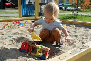 wenig Mädchen Theaterstücke im das Sandkasten mit Spielzeuge. foto