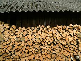 ganze und gehackt Brennholz unter Überhang in der Nähe von ein Holzschuppen gestapelt zum Trocknen foto