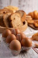 Eier in einer Plastikplatte und Brot, das auf eine weiße Holzplatte gelegt wird. foto