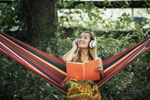 schöne glückliche junge Frau mit Kopfhörern, die Musik hört und ein Buch liest foto