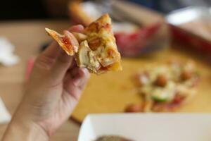 hawaiisch Pizza Dienen auf Holz Tablett mit schmelzen Käse wählen oben nach nehmen ein beißen auf weiblich Hand foto