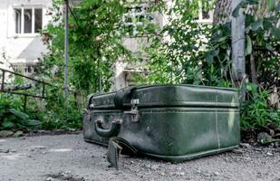 alt Koffer gegen das Hintergrund von ein zerstört Haus im ein verlassen Stadt im Ukraine foto