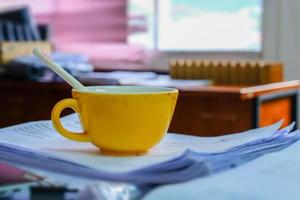 Altes gelbes Glas mit Kaffeeflecken auf Stapelpapieren auf dem Schreibtisch.