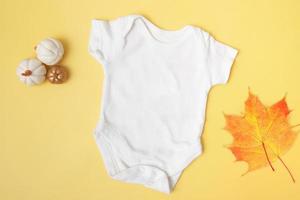 Baby Clobodysuit Mock-up Draufsicht mit Kürbissen und Ahornblättern auf gelbem Hintergrund für Ihren Text oder Logoplatz in der Herbstsaison