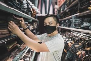junger Mann beim Einkaufen im Modegeschäft mit neuem, normalem Lebensstil, der maskiert trägt foto
