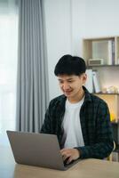 Clever asiatisch Mann mit Hosenträger lächelnd Arbeiten mit Computer Laptop. Konzept Arbeit bilden heim, bleibe beim heim. freiberuflich Leben Stil, Neu normal Sozial Distanzierung Lebensstil. Arbeit bilden irgendwo Konzept. foto