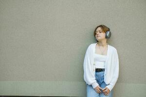 Porträt von ein Teenager Mädchen im Kopfhörer gegen ein grau Mauer. foto