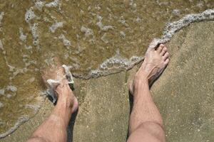 Beine Männer auf das Meer Sand in der Nähe von Meer Welle foto