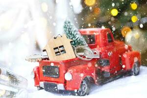 Rotes Retro-Auto mit einem Weihnachtsbaum schmückt mit dem Hausschlüssel im Pickup-Truck zu Weihnachten. Hauskauf, Umzug, Hypothek, Darlehen, Immobilien, Feststimmung, Neujahr foto