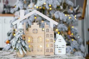 Schlüssel auf Weihnachten Baum und winzig Haus auf gemütlich Zuhause mit Weihnachten Dekor auf Tabelle von festlich Weiß Küche. Geschenk zum Neu Jahr. Versicherung, ziehen um zu Neu Haus, Hypothek, Miete und echt Nachlass foto