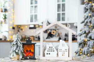 Schlüssel und winzig Haus von ein klein Größe auf gemütlich Zuhause mit Weihnachten Dekor auf Tabelle von festlich Weiß Küche. Geschenk zum Neu Jahr. Versicherung, ziehen um zu Neu Haus, Hypothek, Miete und Kauf echt Nachlass foto