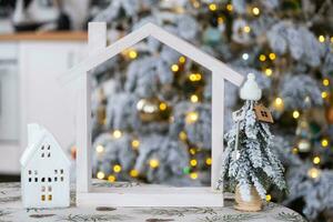 Schlüssel auf Weihnachten Baum und winzig Haus auf gemütlich Zuhause mit Weihnachten Dekor auf Tabelle von festlich Weiß Küche. Geschenk zum Neu Jahr. Versicherung, ziehen um zu Neu Haus, Hypothek, Miete und Kauf echt Nachlass foto