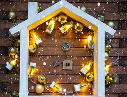 Schlüssel zu Haus mit ein Schlüsselbund winzig Zuhause auf hölzern Hintergrund mit Weihnachten Dekor Layout. Geschenk zum Neu Jahr, Weihnachten. Gebäude, Projekt, ziehen um zu Neu Haus, Hypothek, Miete und Kauf echt Nachlass foto