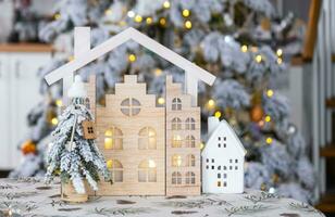 Schlüssel auf Weihnachten Baum und winzig Haus auf gemütlich Zuhause mit Weihnachten Dekor auf Tabelle von festlich Weiß Küche. Geschenk zum Neu Jahr. Versicherung, ziehen um zu Neu Haus, Hypothek, Miete und echt Nachlass foto