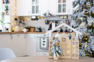 Schlüssel auf Weihnachten Baum und winzig Haus auf gemütlich Zuhause mit Weihnachten Dekor auf Tabelle von festlich Weiß Küche. Geschenk zum Neu Jahr. Versicherung, ziehen um zu Neu Haus, Hypothek, Miete und Kauf echt Nachlass foto