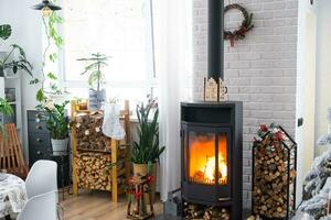 metall schwarz Herd, Verbrennung Feuerstelle Kamin im Weiß festlich Innere von Haus ist dekoriert zum Weihnachten und Neu Jahr, Weihnachten Baum. Brennholz im das Holzstapel, gemütlich und Heizung von Zuhause foto