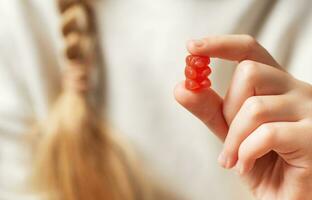 ein Mädchen hält ein gummiartig Bär Vitamine im ihr Hände foto