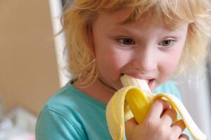 Porträt von ein wenig Mädchen Essen ein Banane. das Konzept von gesund Lebensmittel. ein frisch schnell Snack foto