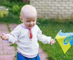 ukrainisch Flagge im das Hände von ein glücklich wenig Kind todler im National Kostüm. lächelnd Kleinkind Mädchen mit das Flagge von Ukraine. ukrainisch Baby macht das zuerst Schritte. foto