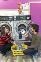 jung Paar ist Putten Kleider im das Waschen Maschine Trommel foto