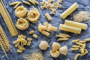 verschiedene Typen von Pasta auf das dunkel Mehl abgestaubt Hintergrund foto