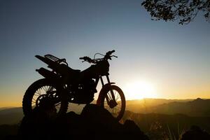 Moto-Cross Fahrrad gegen schön Beleuchtung, Silhouette von ein Moto-Cross Motorrad auf oben von Felsen hoch Berg beim schön Sonnenuntergang, Enduro Motorrad Reise Konzept. foto